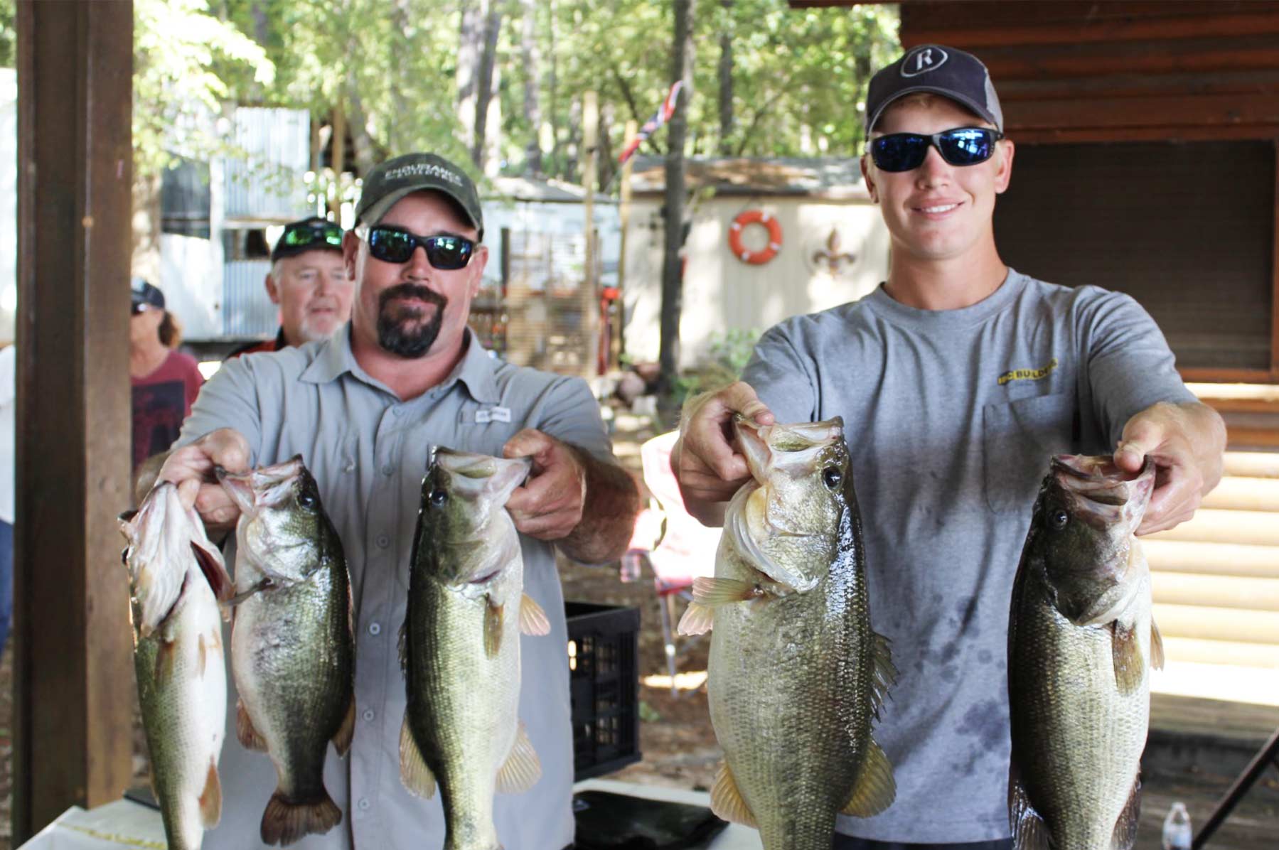 two men in sunglasses and hats holding up five bass fish